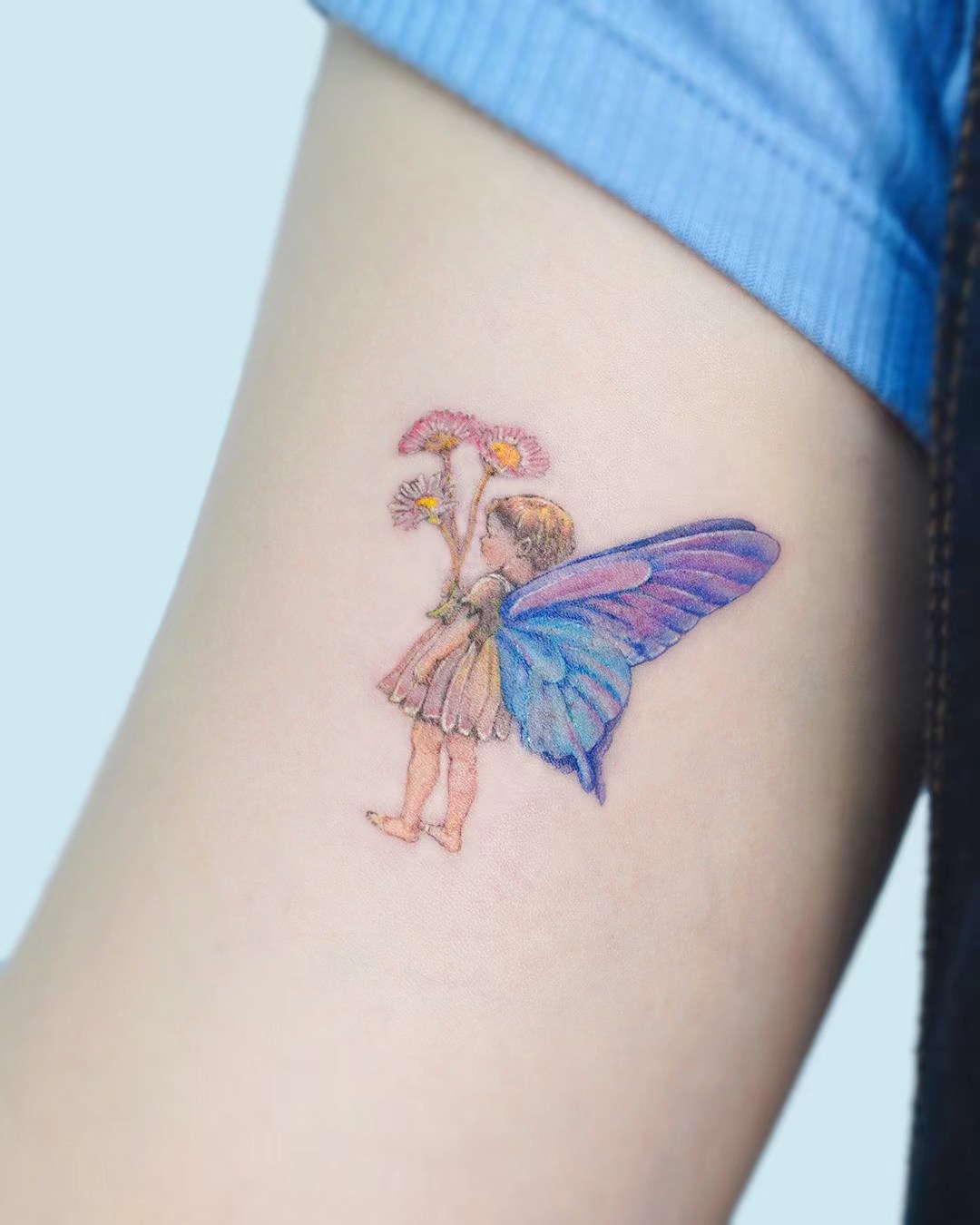 Small fairy tattoo with blue wings on arm